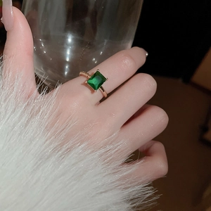 Detail of emerald cut green gemstone ring with twisted gold band on model hand