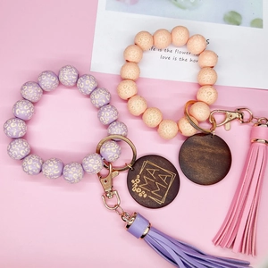 Détail de porte-clés en perles de bois léopard avec pompons en PU et breloque gravée MAMA