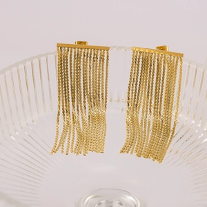 Close-up of gold fringe earrings with long metal chains on a vintage glass vase