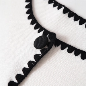 Schicke weiße Strickweste mit schwarzem Kontrastsaum und passendem Stoffknopf-Detail