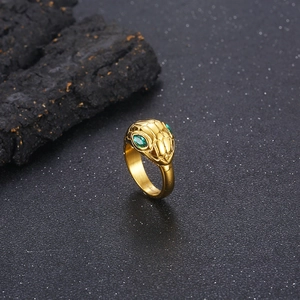 Macro detail of a gold snake ring with green zircon eyes against a dark stone backdrop