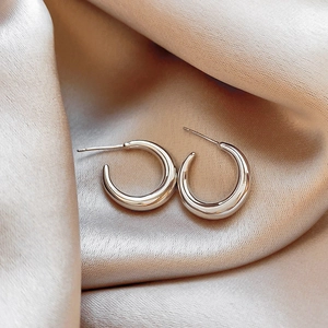 Close-up of polished silver heart-shaped geometric earrings on champagne silk fabric