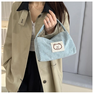 Detail of light blue corduroy square bag featuring a cute bear patch and soft texture