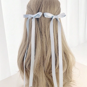 Detail showing two light blue ribbon bow hair clips with long streamers on a model