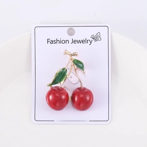 Detail of red cherry brooch with green leaves and gold stem on a white jewelry card