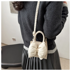 Chic cream bow shoulder bag shown on model with adjustable strap and top handle detail