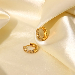 Close-up of small gold hoop earrings with sparkling white zircons on beige silk fabric