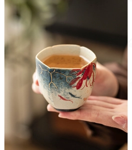 Close-up of hand-held ceramic tea cup with hand-painted koi and lotus patterns