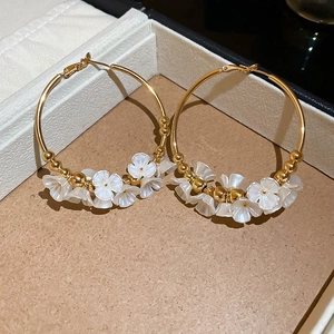 Detail view of large gold hoop earrings with white acrylic flowers in a jewelry box