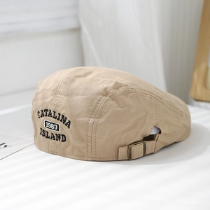 Close-up of 1983 embroidery and adjustable bronze buckle on khaki cotton beret cap