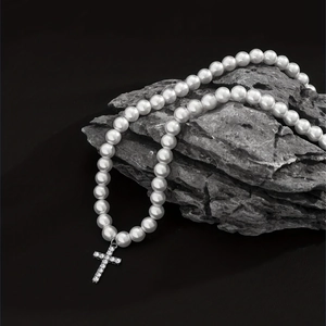 Close-up of pearl necklace with rhinestone cross pendant draped on a dark textured rock