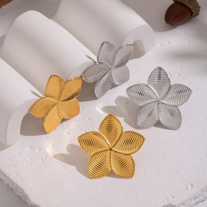 Close-up of textured flower stud earrings in gold and silver finish on white stone