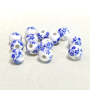 Set of 10mm white ceramic beads with blue floral patterns on beige textile fabric