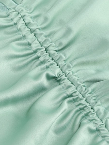 Close-up of mint green satin fabric featuring detailed side ruching and silky texture