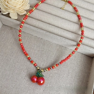 Detail view of 18k gold plated cherry pendant necklace with red beads and faux pearls