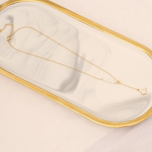 Golden butterfly necklace with white pearls on a marble tray over beige fabric background