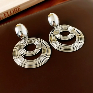 Detail shot of oversized geometric silver spiral earrings on a leather surface