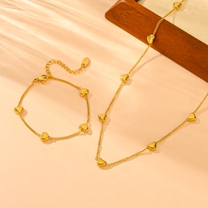 Artistic detail of gold stainless steel heart necklace and bracelet set on a textured surface