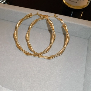 Close-up of large gold twisted hoop earrings with elegant spiral texture on a soft display tray