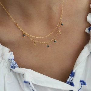 Detail of layered gold titanium necklace with blue beads worn on a floral collar