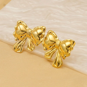 Macro shot of gold bow-shaped stainless steel earrings on a white marble background