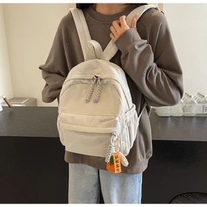 Close-up of beige corduroy backpack with woven carrot charm and multiple pockets