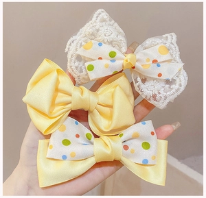 Detailed close-up of three colorful polka dot and satin bow hair clips in hand