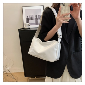 Minimalist white soft leather tote bag worn as a shoulder bag in a neutral studio