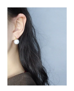 Close-up of elegant gold pearl drop earrings worn by a model against a grey background