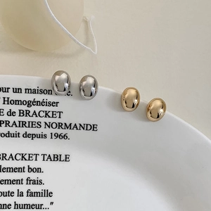 French style polished gold and silver bean stud earrings on a white decorative plate