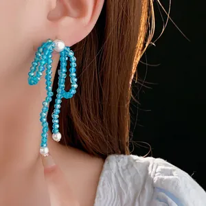 Blue crystal bow tassel earrings with white pearls shown on a model with black background