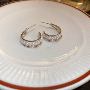 Close-up of silver C-shaped earrings with white pearls on a white ceramic plate