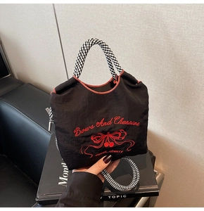 Detail of black nylon tote featuring red cherry embroidery and checkered straps