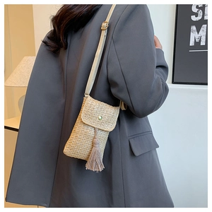 Detail of beige woven straw crossbody phone bag with fringe tassels and long strap