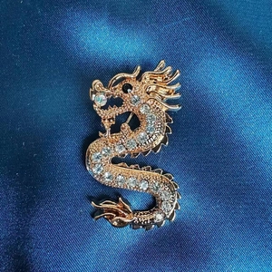 Detail einer goldenen Drachenbrosche mit klaren Kristallen auf dunkelblauem Seidenstoff