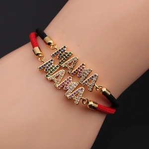 Detail eines MOM-Anhängers mit Regenbogen-Zirkonia an einem rot-schwarz gewebten Armband