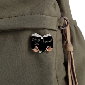 Detail of Sorry I'm Booked book brooch with gold plating on olive canvas backpack