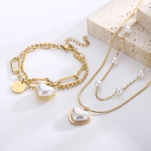 Detail view of double-layer gold necklace and bracelet with heart pendants and pearls