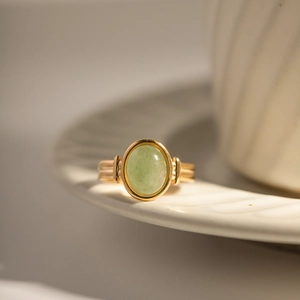 Macro detail of gold oval green gemstone ring on white textured ceramic vessel