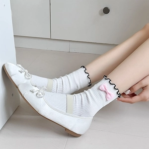 Detail of white cotton slouch socks with black wavy edges and pink bows on feet
