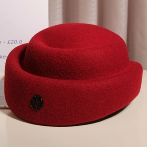 Close-up of a red wool felt pillbox hat with a metal M emblem and rolled edge details