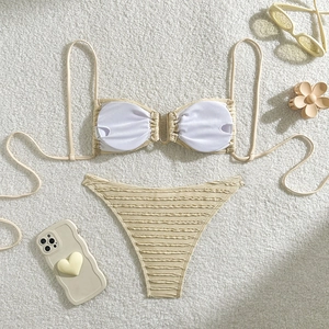 Flat lay of a beige textured bikini set with metal buckle on a white plush carpet