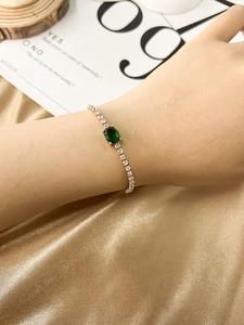 Detail of gold bracelet with green oval gemstone and white zircon on silk background