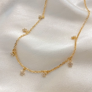 Detail of gold necklace with six cubic zirconia flower pendants on soft silk fabric