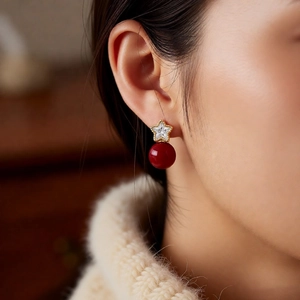 Detail of 18K gold star pearl earrings with deep red beads worn on a model with knitwear