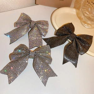 Detailed view of silver and gunmetal rhinestone bow hair clips on a cream surface