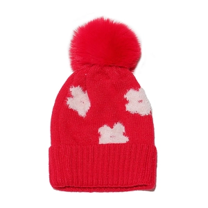 Detail of red knit hat featuring a fluffy faux fur pompom and soft white floral patterns