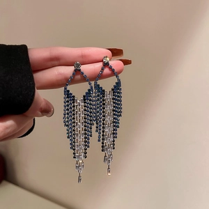 Close-up of blue and silver rhinestone tassel earrings held against a neutral wall