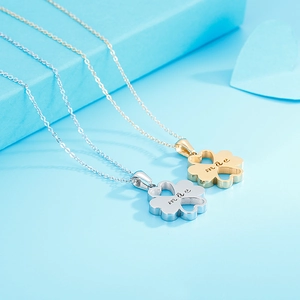 Close-up of silver and gold clover necklaces with mae engraving on blue heart background