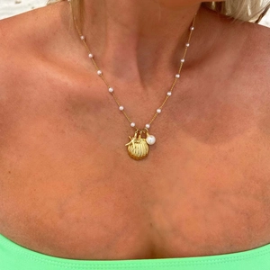 Dettaglio di una collana a conchiglia dorata con ciondoli a stella marina e perle su modella